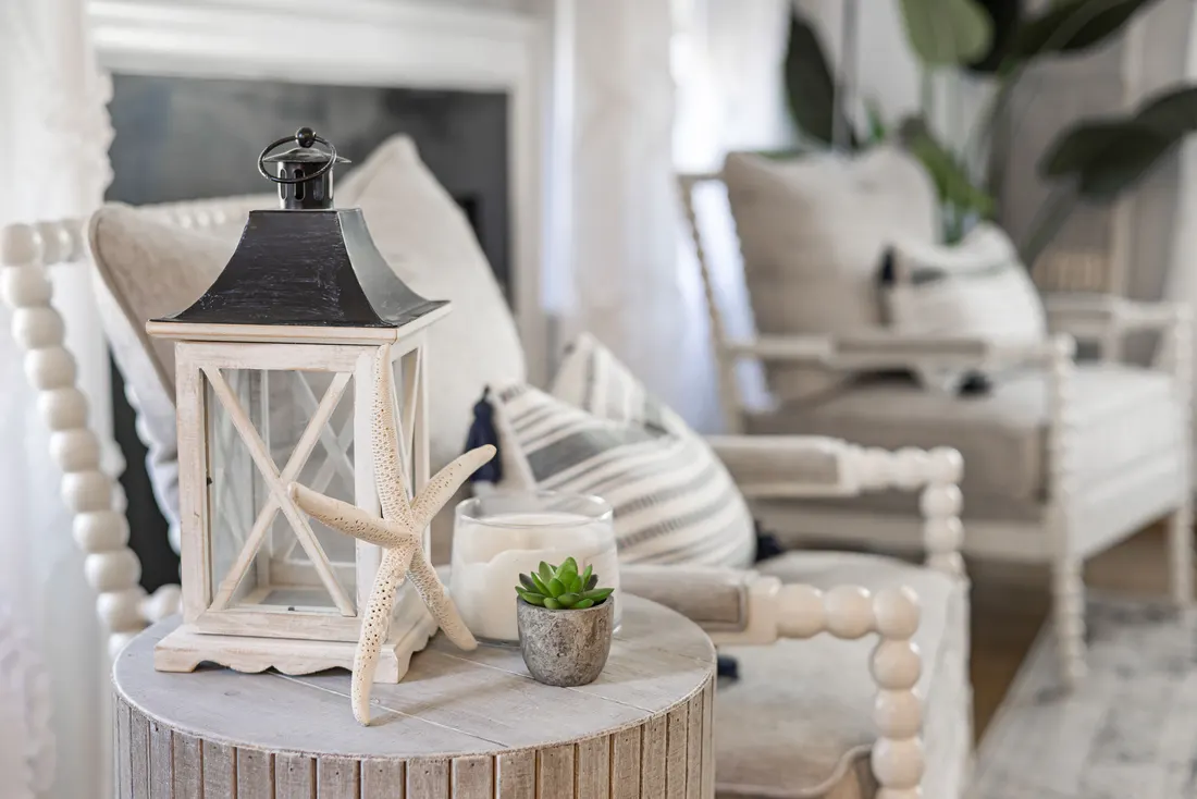 A tidy, bright living room with white chairs, a lantern and a starfish on a side table